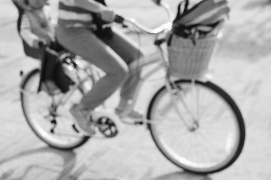 Defocused silhouette of active mother and child riding a bike together on oudroors background. Back side view image