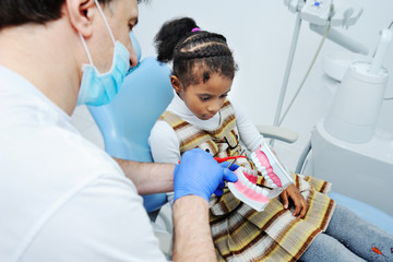 dentist tells African girl child how to properly brush their teeth. Oral hygiene. African-American, dentistry, tooth decay