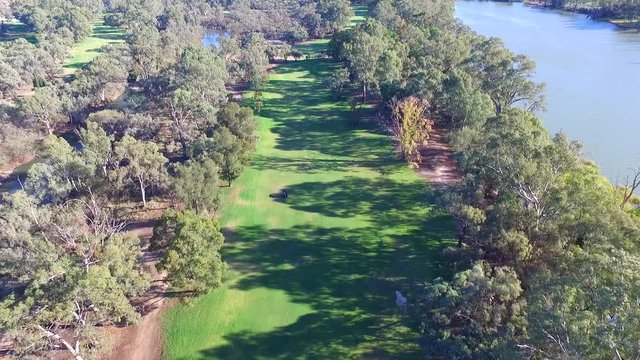 Aerial view of Golfers in electric Golf Buggy with Caddy driving through bush land Golf Course by river.