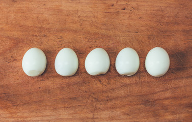 five cooked peeled eggs in a row on an old cutting board. view from above close-up, toning photo