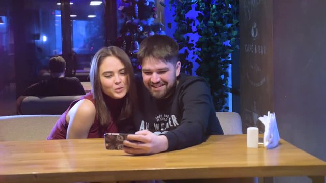 Attractive couple having fun, laughing, showing tongue using smartphone. 4K