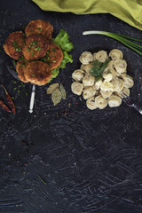 Fried cutlets and russian pelmeni on black background
