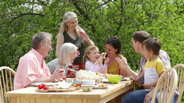 Family are sitting outdoors in summer to have a picnic meal.