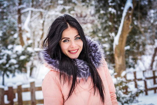 Brunette girl standing on the background of snow and trees and smiling