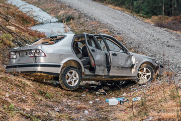 Silver colored stolen car that have been crashed and ditched on the side of a dirt road. Totally vandalized and wrecked.