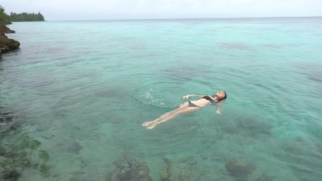 Young woman in black swimsuit is swimming into clear water of caribbean sea