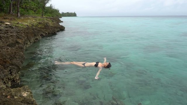 Young woman in black swimsuit swims at clear water near the coastline of caribbean sea