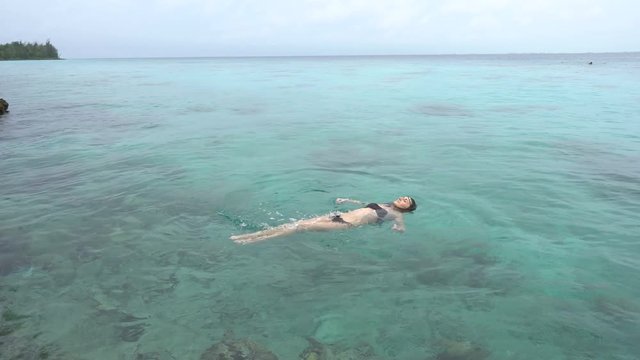 Young woman in black swimsuit swims at clear water of caribbean sea