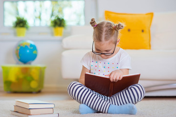 Portrait of clever little girl sitting with book on the floor