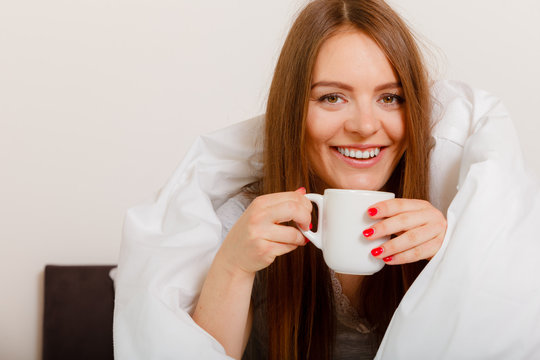 Smiling woman holding cup of drink in bed
