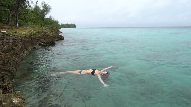 Young slender woman in black swimsuit is lying on the water of caribbean sea