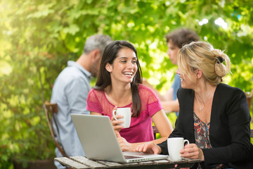 Two women friends sitting at a terrace cafe using a laptop