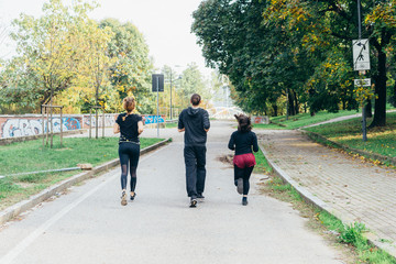 Three women and man runners from back running outdoor in city park in autmun - runners, training, athlete concept