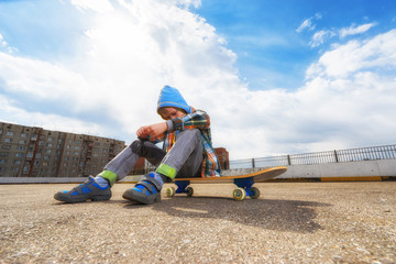 Boy on the street  sitting on skateboard and thinking about something.