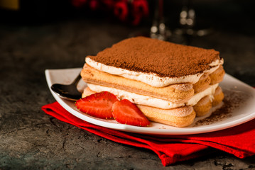 Tiramisu with strawberry on the table. Valentines concept. Dark moody style.