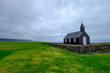 Black Icelandic church in a field of grass under a cloudy sky