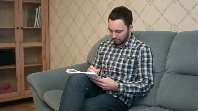 Young man sitting on the couch making some notes in the textbook
