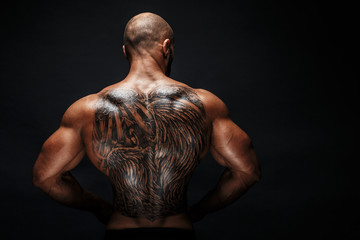 Unrecognizable muscular man with tattoo on back against of black background. Isolated.