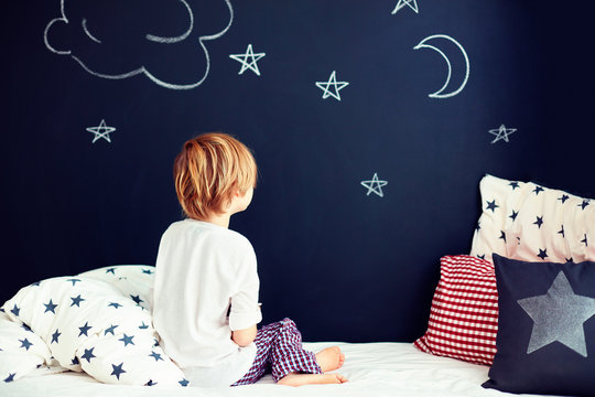 cute kid in pajamas dreaming , while sitting in bed