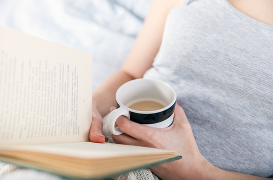 Girl reading book and drinking coffee in bed at home