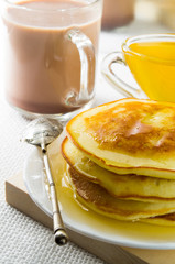 Glass mug with cocoa, silver spoon, honey and pancakes