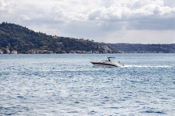 Obraz premium Luxury yacht / boat crosses Bosphorus between European and Asian sides in Istanbul. It is cloudy autumn day. It is internationally-significant waterway located in northwestern Turkey