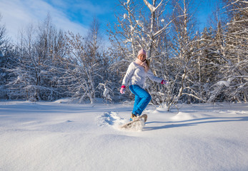 Winter sport activity. Woman with snowshoes on fluffy snow in forest. Beautiful landscape with coniferous trees and white snow.