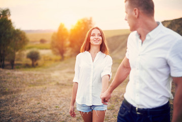 Obraz premium Happy couple holding hands and walking together outdoors at sunset