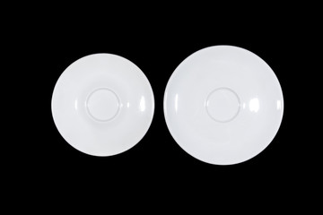 Two flat white saucers side by side smaller and bigger on black background directly from above
