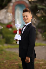 Piękny uśmiechnięty chłopak trzyma w ręku świece na tle kaplicy. - obrazy, fototapety, plakaty