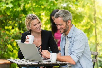 A smart couple is sitting at a terrace cafe and using a laptop