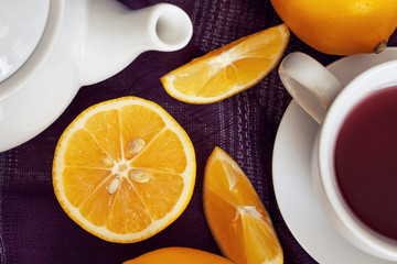Lemon on purple tablecloth with cup of tea and teapot. Top view