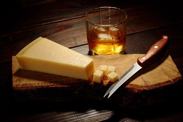 Parmesan cheese cut into cubic on a wooden board with knife and glass of whiskey on the second plan with ice © vania_zhukevych
