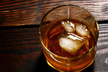Overhead shot of glass of whiskey with ice on wooden table