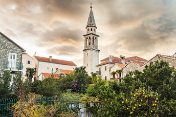 Old tower in retro vintage style among city garden in old European town in front of dramatic sky during sunset