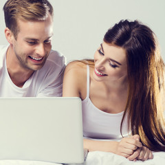 Couple using laptop, on bed