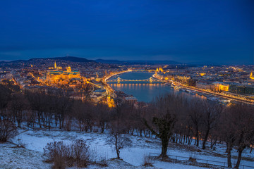 Budapest, Hungary - Panoramic skyline view of the Buda Castle (Royal Palace), Chain Bridge, Danube River and the Parliament at blue hour as seen from Gellert Hill in winter time