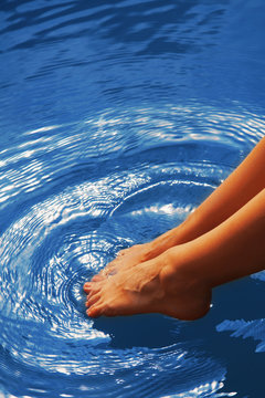 Relaxation. Young woman wets feet in water. (Sea, ocean, travel)