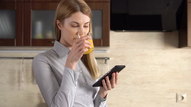 Beautiful young woman with a phablet standing in kitchen. Browsing Internet and smiling.