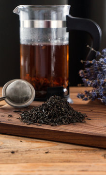 A composition of a tea ball, french press, dry black tea leaves and lavender on wooden board. Vertical