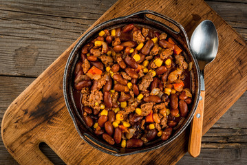 Traditional Mexican and Chilean dish of chilli con carne. In the rustic pan, next to tortillas and fresh vegetables on a wooden table, copy space
