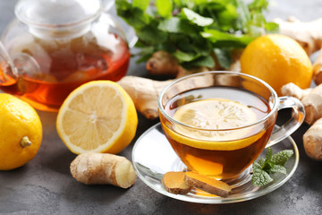 Cup of tea with ginger root and lemon on grey wooden table