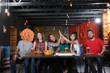 Cheerful friends watching soccer game in sport bar