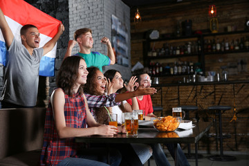 Cheerful friends with France flag emotionally watching soccer game in sport bar