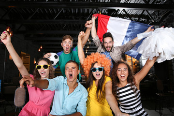 Fototapeta premium Cheerful friends with France flag emotionally watching soccer game in sport bar