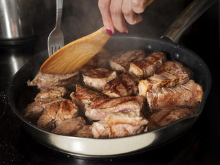 A woman flipping steaks on a frying pan.