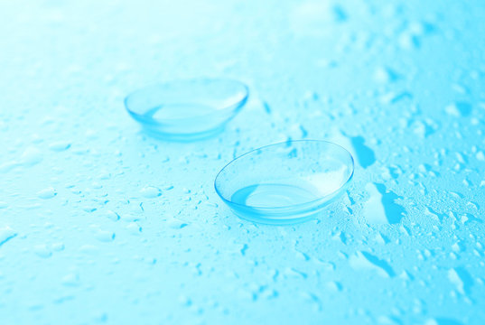 Pair of contact lenses and drops of solution on blue background, close up view