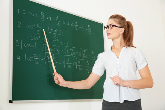 Young teacher with pointer beside blackboard on white background