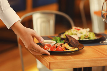 Waiter serving meals in restaurant, close up