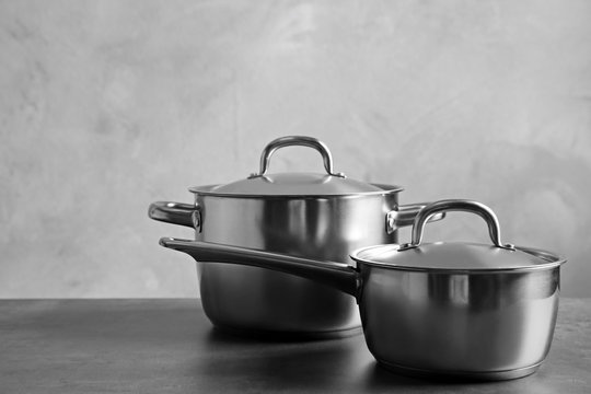 Kitchenware concept. Stainless saucepans on table and grey textured background